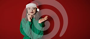 Merry surprised young woman wear xmas sweater Santa hat posing pointing hands arms aside indicate on workspace area isolated on