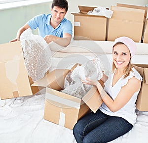 Merry young couple unpacking boxes with glasses