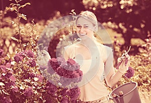 Merry young woman working with bush roses with horticultural too