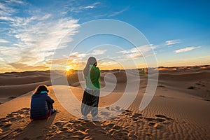 Merzouga, Morocco - October 16, 2018: Two women watching a beautiful sunrise over Erg Chebbi sand dunes near Merzouga, Morocco