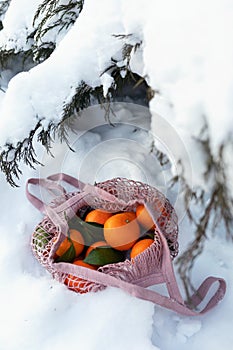 Mesh bag with tangerines in the snow under the Christmas tree