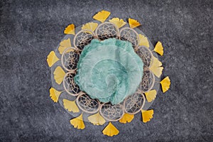 Mesh basket with a green rug and yellow leaves on a gray graphite background, a nest for shooting