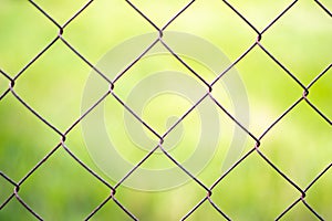 Mesh cage in the garden with green grass as background. Metal fence with wire mesh. Blurred view of the countryside through a