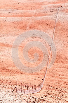 A mesh fence traverses a J-shaped desert rocky hilly area