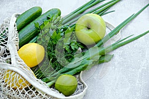 Mesh grocery bag with healthy organic food, vegetables and fruits on stone background. Top view produce bag with cucumbers,