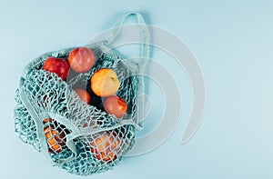 Mesh shopping bag with fruits plims and peach on blue background. Zero waste, eco friendly concept