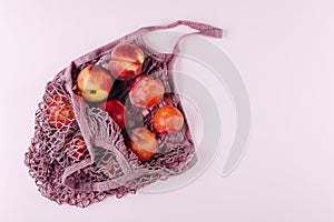 Mesh shopping bag with fruits plims and peach on pink background. Top view, flat lay