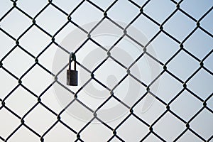 Mesh wire fence with lock on the sky background.