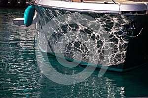 The mesmerizing reflection of the water on the glossy side of a huge yacht anchored, chrome details