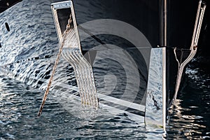 The mesmerizing reflection of the water on the glossy side of a huge yacht anchored, chrome details, chains and ropes to
