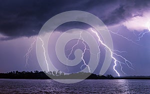 Mesmerizing shot of multiple lightning strikes by a river with a dark blue sky