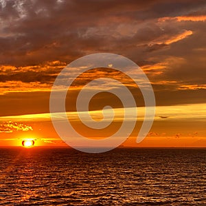 Mesmerizing view of a calm sea with sunset sky and the bright sun is seen over the clouds