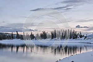 Mesmerizing view of lake water reflecting forest trees covered with snow on a cold winter day