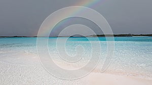 Mesmerizing view of a tropical beach and shallow water, with a rainbow and cloudy sky over the sea