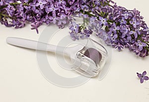 Mesoroller and lilac flowers on a white background. Concept of skin care, anti-wrinkle, Spa