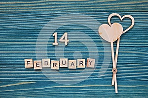 Message `14 February` made from wooden tiles and two love hearts on a blue background