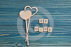 Message `Be mine` made from wooden tiles and two love hearts on a blue background