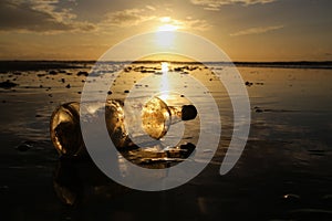 Message in a bottle at the beach. Beautiful sunset with sun reflections in the sand