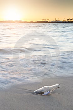 Message in bottle on beach with sunset and blur industry background.