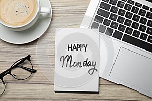 Message Happy Monday written in notebook, laptop and cup of coffee on wooden desk, flat lay