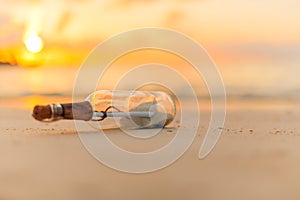 Message with letter inside the bottle on a beach in sunset