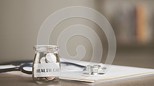 message on paper and coins in glass jar, stethoscope and medical report, all on table, savings concept, for health care expenses,