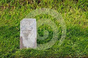 Message with Please keep a safe distance on the grunge metal board standing on the green grass. New normal social