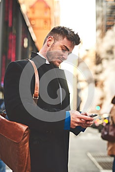 The messages keep coming. a young well dressed man texting on his cellphone while waiting for a taxi to get him to work