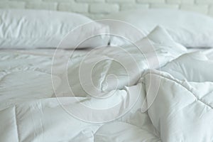 Messed bed with white pillow and blanket with natural light in bedroom in the morning