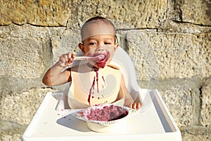 Messy baby boy eating blueberry cake with spoon