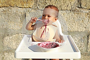 Messy baby boy eating blueberry cake with spoon