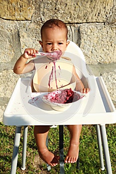 Messy baby boy eating blueberry cake with spoon