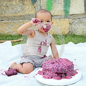 Messy baby boy eating first birthday cake with spoon
