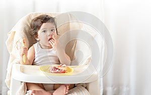 Messy baby girl eating cake.  Lovely infant girl holding a spoon, enjoying eating cake