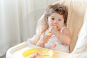 Messy baby girl eating cake.  Lovely infant girl holding a spoon, enjoying eating cake