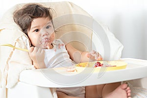 Messy baby girl eating cake.  Lovely infant girl holding a spoon, enjoying eating cake