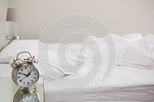 Messy bed with alarm clock on bedside table
