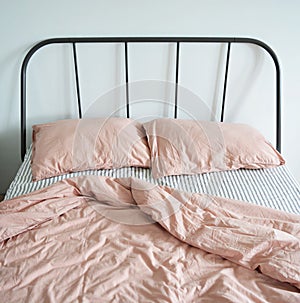 Messy bed with pink linen pillows, blanket and striped sheet