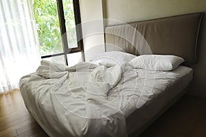 The Messy bed and White pillow with blanket on bed unmade. Concept of relaxing after morning with window background