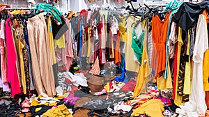 Messy clearance section in a clothing store, with colorful garments on racks and on the floor
