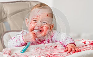 Messy and dirty baby is eating from spoon photo