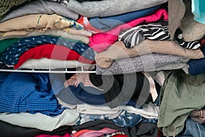Messy folded clothes crammed in a closet on a shelf. Depicting woman`s wardrobe, consumerism, cleaning up, tidying up, purging, et photo