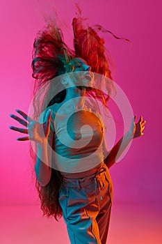 Messy hair. Young girl expressing emotions, shouting, screaming and laughing against pink studio background in neon