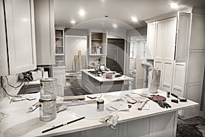 Messy home kitchen during remodeling with cabinet doors open cluttered with paint cans, tools and dirty rags