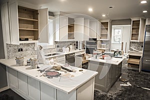 Messy home kitchen during remodeling with cabinet doors open cluttered with paint cans, tools and dirty rags, canned ceiling light photo