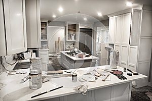 Messy home kitchen during remodeling with cabinet doors open cluttered with paint cans, tools and dirty rags photo