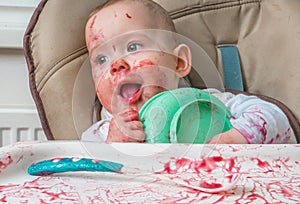 Messy little baby is eating dinner from bowl