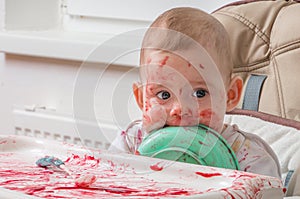 Messy little baby is eating snack and licking bowl