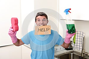 Messy man in stress in washing gloves holding sponge and detergent spray bottle asking for help