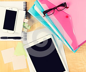 Messy office table with digital tablet, smartphone, reading glasses, notepad and filling folders. View from above